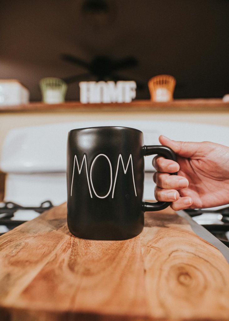 Crop anonymous person taking black ceramic mug with white word Mom placed on wooden table in living room